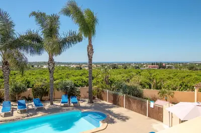 a swimming pool with chairs and palm trees at Casa Laranjal in Albufeira