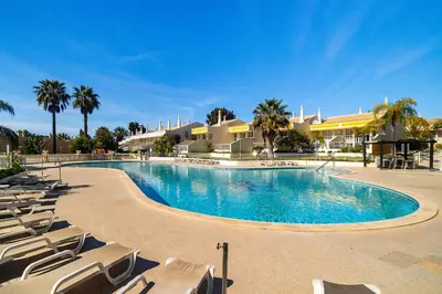 a large swimming pool with chairs and palm trees at Ponta Grande Resort - Villa Solmar in Albufeira