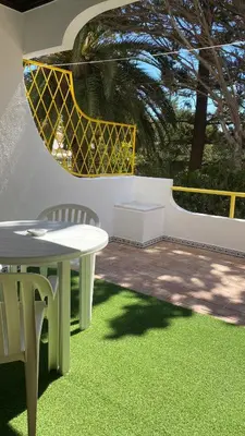 a patio with a table and chairs and grass at Apartamento 5 min a pé da praia, com terraço ao sol, no 1º andar in Quarteira