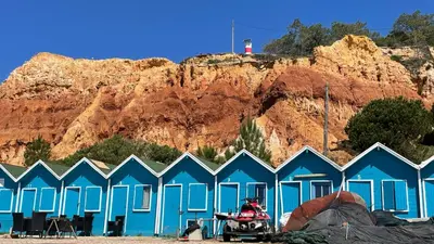 a group of blue beach huts in front of a mountain at Noly by Check-in Portugal in Albufeira