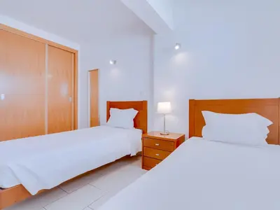 two beds in a bedroom with white sheets and a night stand at AL - Apartamento Canto do Mar frente à praia in Quarteira