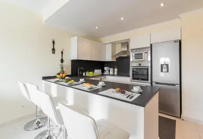 a kitchen with white cabinets and a counter with chairs at Vista Das Ondas 308 By RS in Olhos de Água