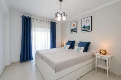 a bedroom with a bed with blue curtains at Mello Apartamento renovado, praia de Quarteira in Quarteira