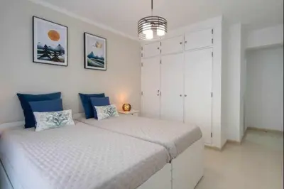 a white bedroom with two beds with blue pillows at Mello Apartamento renovado, praia de Quarteira in Quarteira