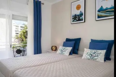 a bedroom with two beds with blue curtains and a window at Mello Apartamento renovado, praia de Quarteira in Quarteira