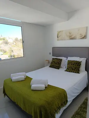 a white bedroom with a large bed with a green blanket at Paradise Near Old Town in Albufeira