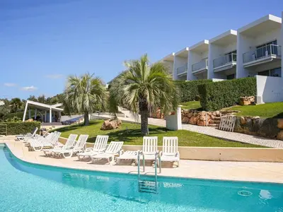 a pool with chairs and palm trees and a building at Serenity 09 House by Stay ici Algarve Holiday Rental in Albufeira