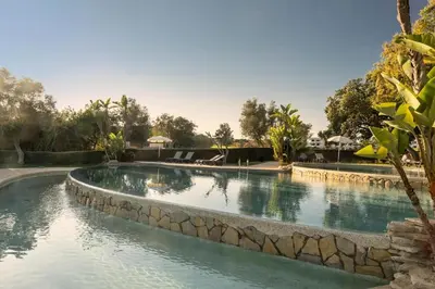 a swimming pool with a stone wall around it at Balaia Golf Village T2 a 10 minutos da praia in Olhos de Água