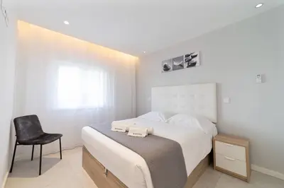 a white bedroom with a bed and a chair at Saro Apartment by HelloVacations in Albufeira