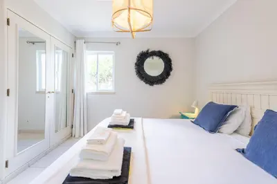 a bedroom with a white bed with blue pillows and a mirror at Jardins do Golfe at Vale do Lobo in Vale do Lobo