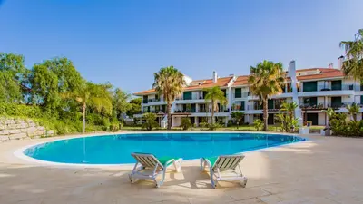a swimming pool with two chairs and a building at SomeSunnyDay Vila Sol Village in Quarteira