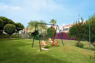 a swing set with two chairs in a yard at Apartamento Condomínio Montechoro by CM Properties in Albufeira