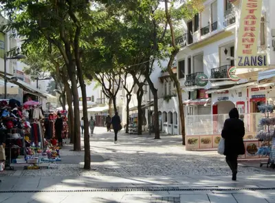 a woman walking down a street with trees and shops at OldTownPool Albufeira in Albufeira
