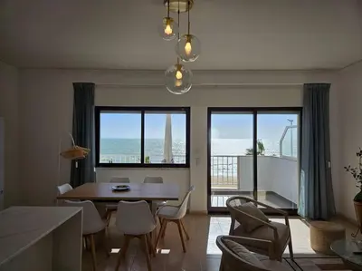 a living room with a table and chairs and the ocean at Apartamento moderno na praia com varanda grande in Quarteira