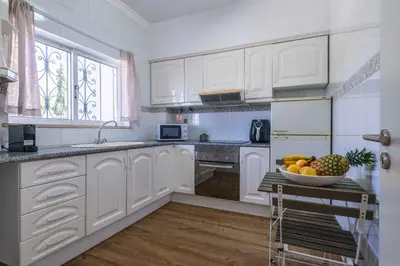 a kitchen with white cabinets and a bowl of fruit on a table at São Rafael 1 Bedroom with Pool in Albufeira