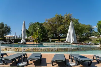 a pool with chairs and umbrellas in front of it at Luxury Beach House Apartment - Golf & Tennis Court & Pool View in Albufeira