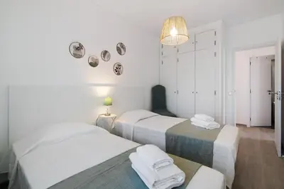 a white bedroom with a bed and a chair and a window at Justo's House in Faro