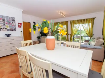 a kitchen and dining room with a white table with yellow flowers at Quinta do Paiva Apartment by Stay ici Algarve Holiday Rental in Albufeira