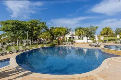 a swimming pool in a park with chairs and trees at Albufeira Club 109 in Albufeira