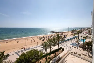 a beach with people and umbrellas and the ocean at Beachfront Apartment T2 in Quarteira