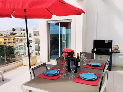 a dining table with a red umbrella on a balcony at Sol Mar Penthouse by Da Costa in Albufeira