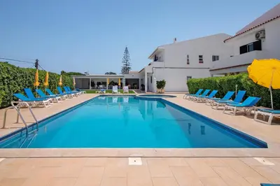 a swimming pool with blue chairs and umbrellas at Mira Parque Apartamentos in Albufeira