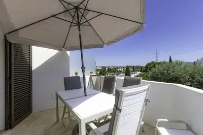 a white table and chairs with an umbrella on a balcony at CLUB ALBUFEIRA - 2 bedroom apartment, air conditioning and pools in Albufeira