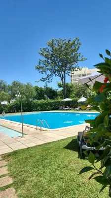 a blue swimming pool with a tree and a building at The Navigator Olympus in Quarteira