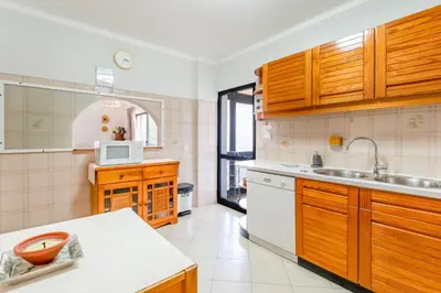 a kitchen with wooden cabinets and a sink at 2 BDR Flat With Pool in Vilamoura by LovelyStay in Quarteira