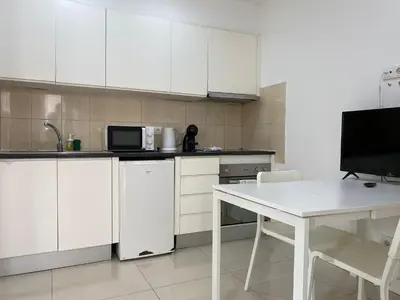 a kitchen with white cabinets and a table and a tv at By the Sea Apartments B3 in Albufeira