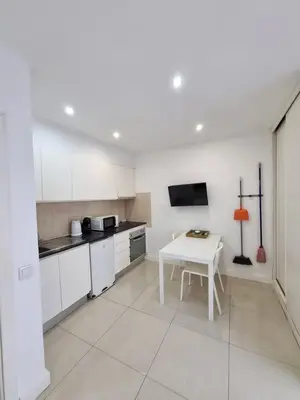 a kitchen with white cabinets and a table and a tv at By the Sea Apartments B3 in Albufeira