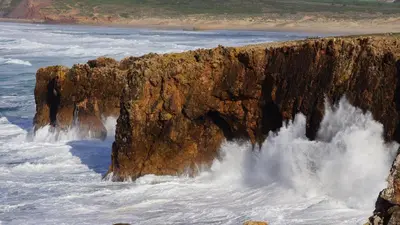 a rock cliff in the ocean with water crashing onto it at Charming House in Albufeira with Shared Pool in Albufeira