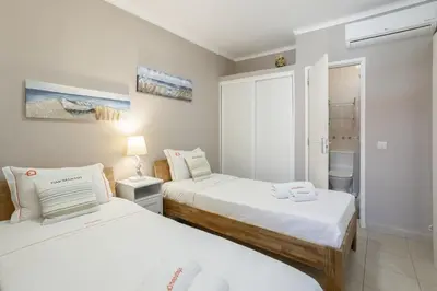 a bedroom with two beds and a bathroom with a window at Forte Beach Retreat - 2BR Apartment with Terrace & AC in Caliços