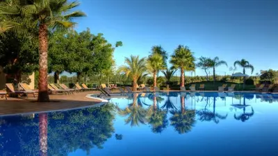 a pool at a resort with palm trees and chairs at VILAMOURA - The Residences in Quarteira
