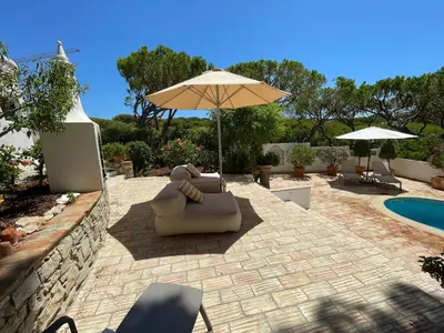 a patio with an umbrella and chairs and a pool at Vila Antic in Almancil