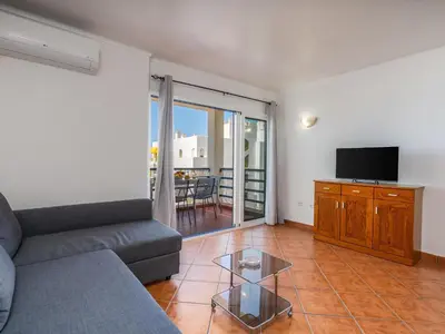 a living room with a couch and a flat screen tv at T1 com Varanda e vista mar a 200m da Praia in Quarteira
