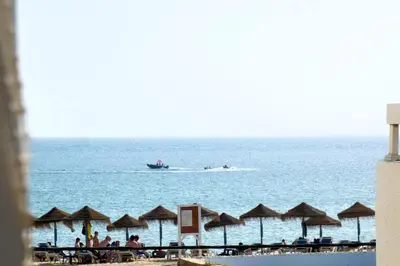 a boat in the water near a beach with umbrellas at Encanto da Ria in Faro