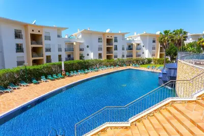 a swimming pool with chairs and umbrellas next to a house at BnB Homes Eco Apartment with Terrace, 2 Swimming pools & Tennis court in Albufeira