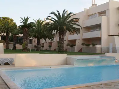 a swimming pool in front of a building with palm trees at Akisol Vilamoura Rise in Quarteira