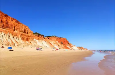 a beach with people on the sand and cliffs at Windmill Hill Cozy Townhouse by BeCherish in Albufeira