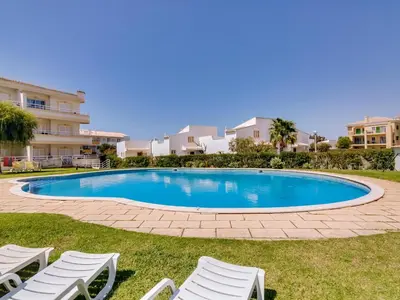 a swimming pool with lawn chairs and condos at Apartamento JV com 2 quartos e piscina, Vilamoura in Quarteira