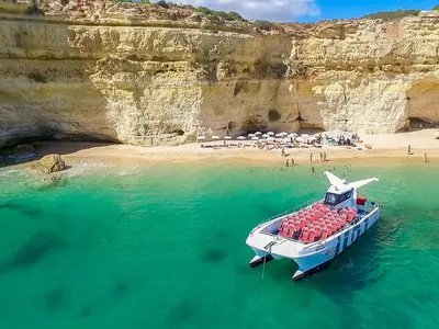 a boat in the water next to a cliff at Ocean Breeze Rooms, Albufeira in Albufeira