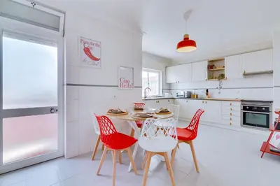 a white kitchen with a table and red chairs at Brisa Algarvia 1 in Faro