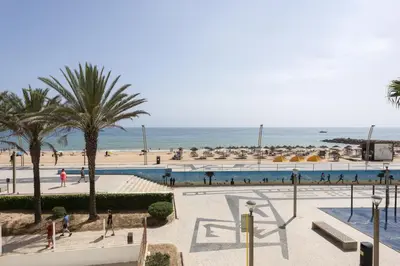 a group of people walking around a swimming pool next to the beach at Mare Viva - Seafront with pool by HD in Quarteira