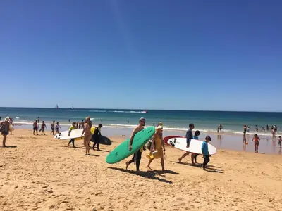 a group of people walking on the beach with surfboards at Os Apartamentos A Ramos na Praia da Galé Estão inserido em Condomínio com PISCINA, Fica apenas a 350 Metros da Praia da Galé - Apartamentos com Ar Condicionado tanto nos Quartos como na Sala, Smart TV com Prime Vídeo e Cozinha Completa in Albufeira