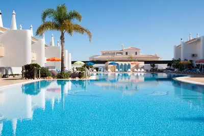 a large swimming pool with a palm tree and buildings at Os Apartamentos A Ramos na Praia da Galé Estão inserido em Condomínio com PISCINA, Fica apenas a 350 Metros da Praia da Galé - Apartamentos com Ar Condicionado tanto nos Quartos como na Sala, Smart TV com Prime Vídeo e Cozinha Completa in Albufeira