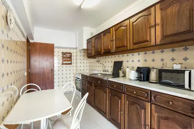 a kitchen with wooden cabinets and a white table at Amoreira 3br City Center at Homesbyfc in Faro