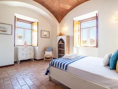 a bedroom with a bed and two windows and a chair at Casa Algarvia Senhorial by Stay ici Algarve Holiday Rental in Albufeira