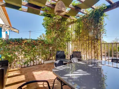 a patio with a table and chairs and vines at Vivenda Pereiras com 2 quartos em Quarteira in Quarteira