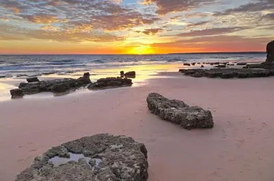 a sunset on a beach with rocks in the sand at Sunny Terrace facing the pool and barbecue by Algarve Dream Holidays in Guia